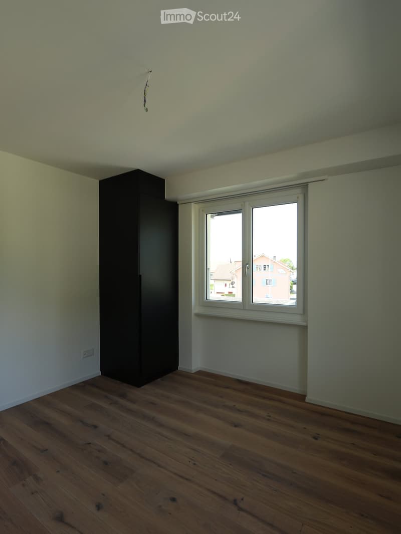 Unfurnished Room. Empty room with wooden flooring, light-colored walls, and a single window with white frame. A dark-colored cabinet is positioned against one wall.