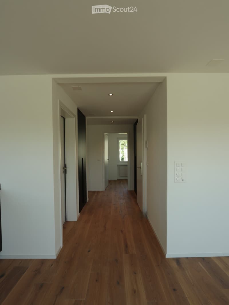 Corridor / Hallway. Empty hallway with wooden flooring, white walls, and recessed lighting. Doors lead to adjacent rooms.