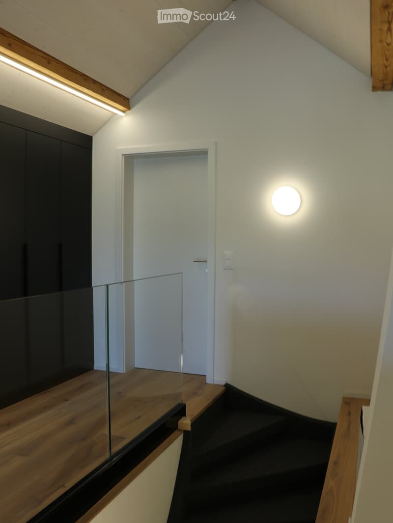 Modern hallway with wooden flooring, glass railing, and recessed lighting. Features a white door and a sleek, minimalist design.