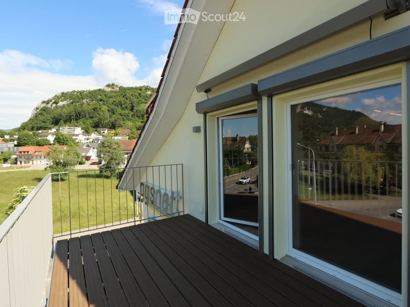 Balcony with wooden decking, metal railing, large windows, and scenic view of greenery and houses.