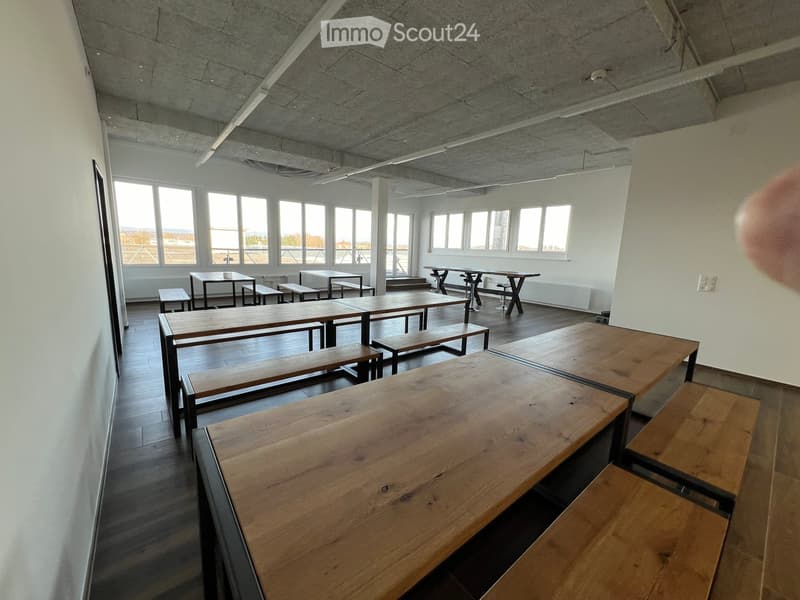 Bright, open room with large windows, wooden tables, and benches arranged for seating.