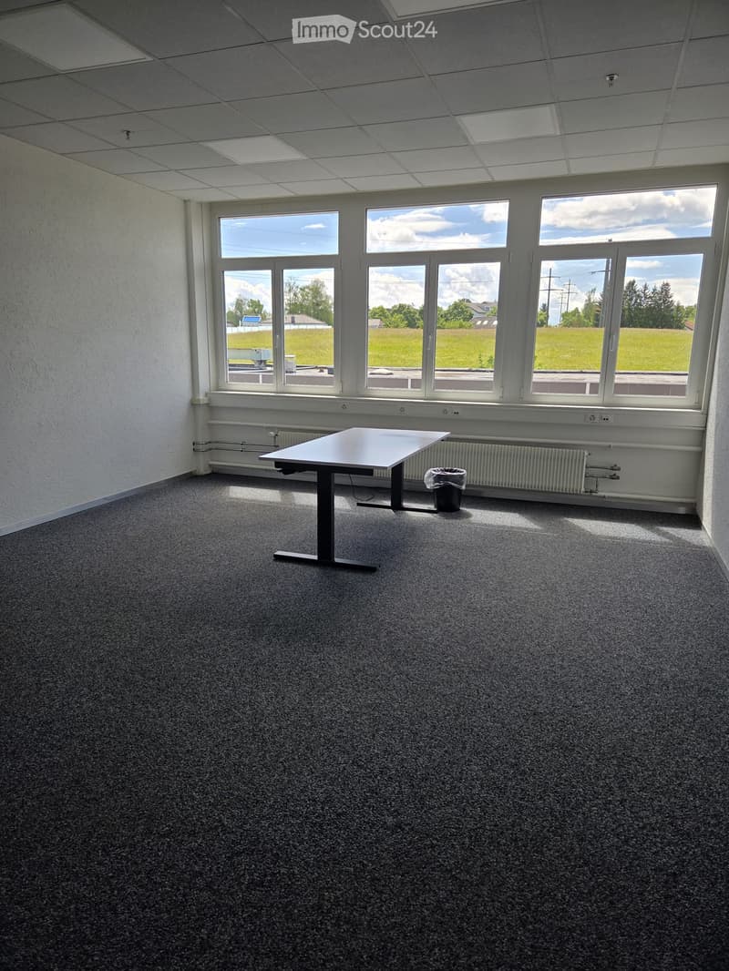 Empty room with carpeted floor, large windows, and a single table.