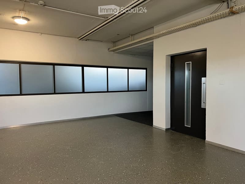 Empty room with white walls, grey speckled floor, large window with frosted glass panels, and a black door with a silver handle.