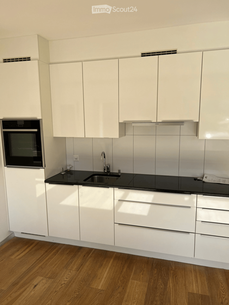 Kitchen. Modern kitchen with white cabinets, black countertops, and a wooden floor. Features an oven, sink, and faucet.
