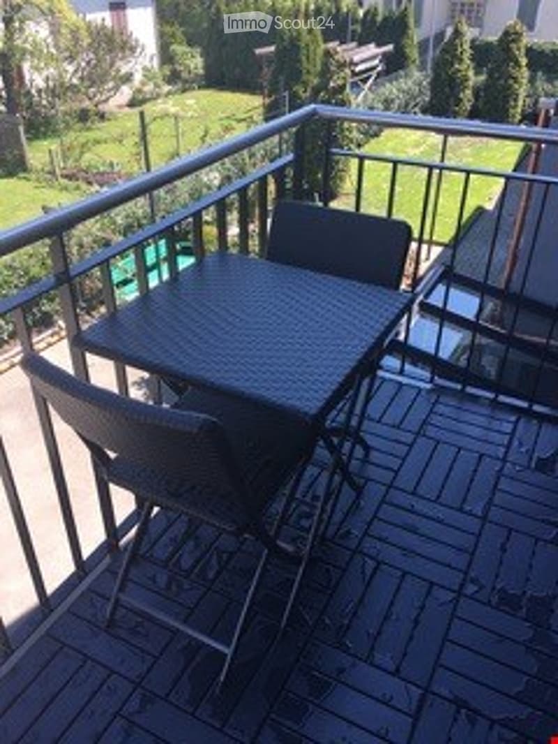 Balcony with wooden decking, metal railing, and outdoor furniture including a table and chairs.