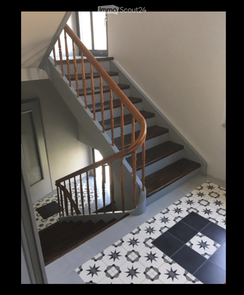 Spiral staircase with wooden handrail and steps, leading to an upper level. The hallway features patterned tiles with star and geometric designs.