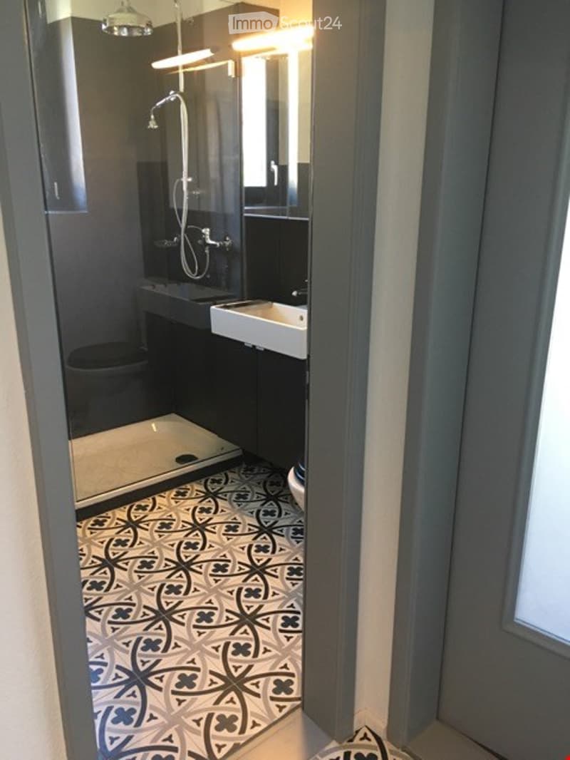 Modern bathroom with a white sink, toilet, and glass-enclosed shower. The floor features a black and white patterned tile design.