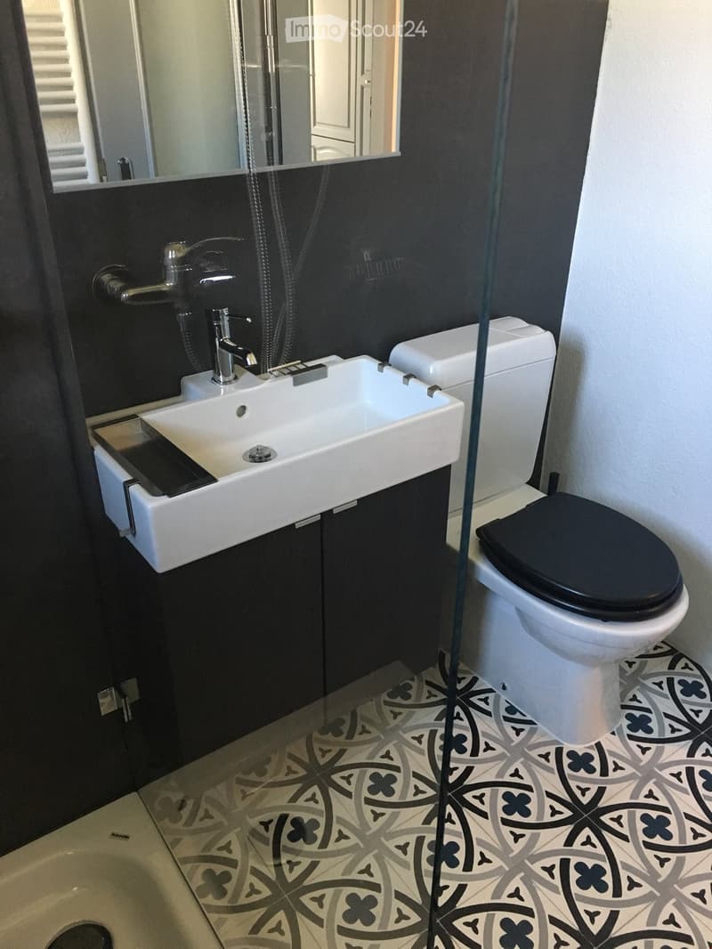 Modern bathroom with a white sink, chrome faucet, toilet with black seat, and decorative patterned tiles on the floor.