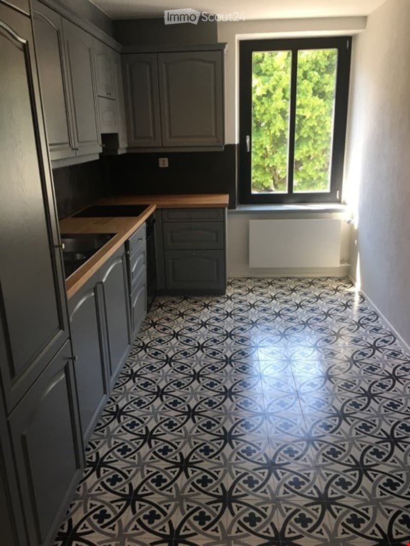 Modern kitchen with grey cabinets, wooden countertops, and a black and white patterned tile floor. A large window provides natural light.