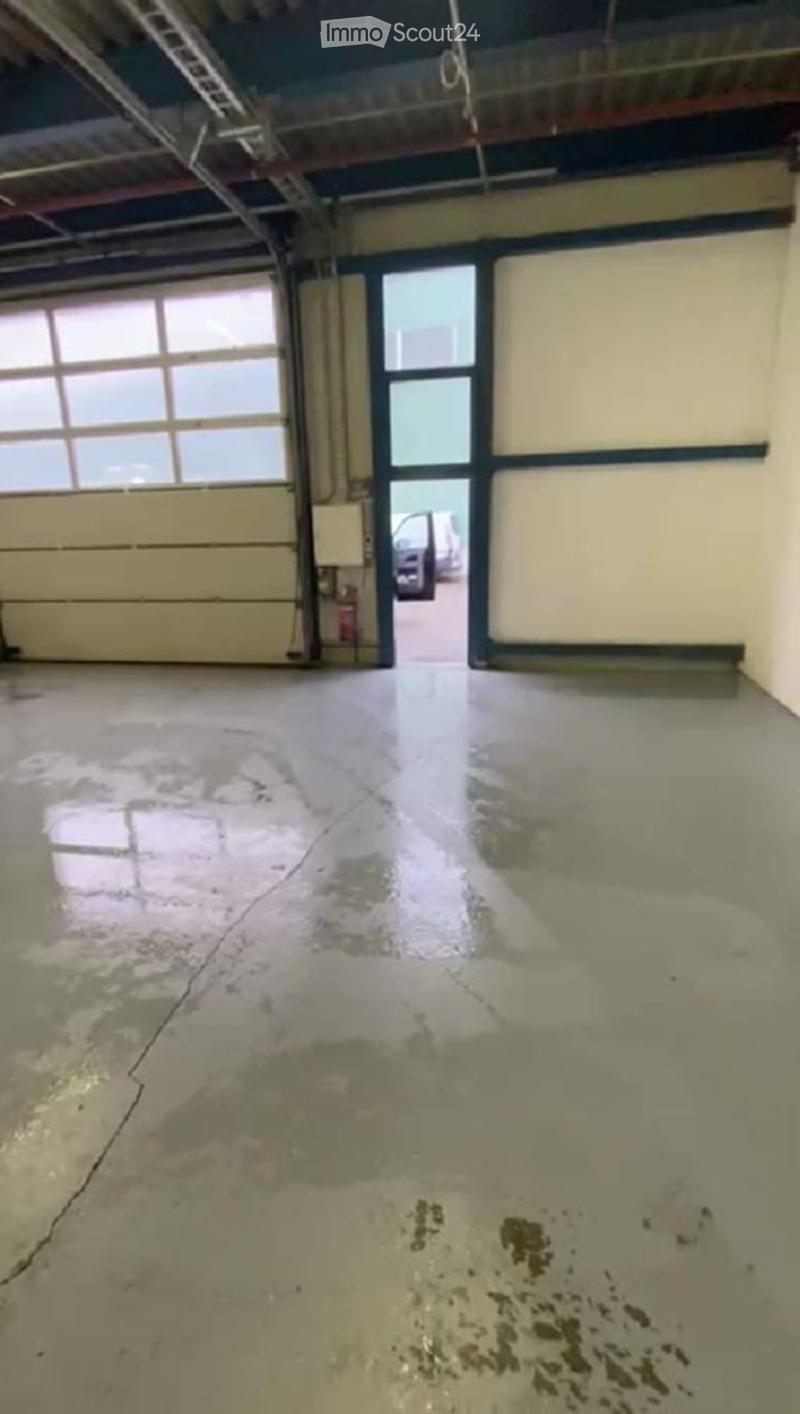Empty garage with large roll-up door, concrete floor, and visible cracks and stains. No furniture or equipment present.