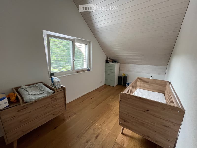 Bright, airy bedroom with wooden cribs, changing table, and a small drawer unit. Large window with blinds offers natural light.