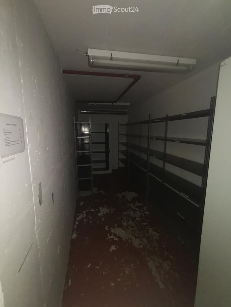 Empty corridor with metal shelving units on the right side, white walls, and a worn floor.