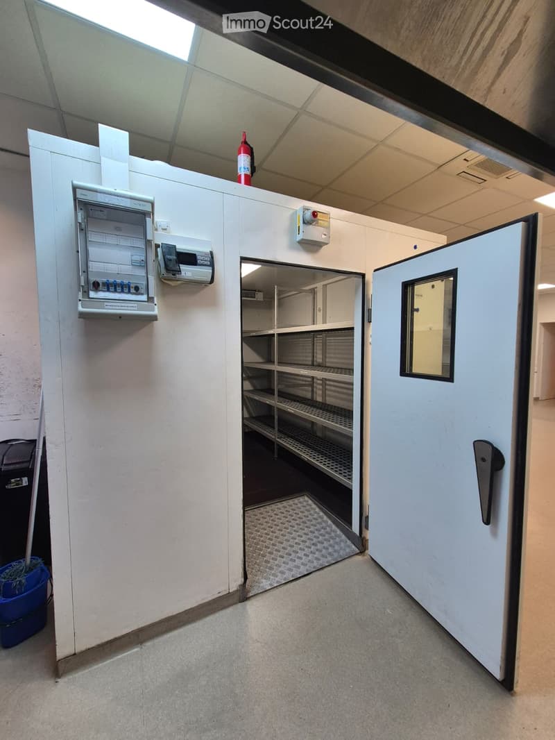The room is storage room with metal shelves and floor, door and electrical switches.