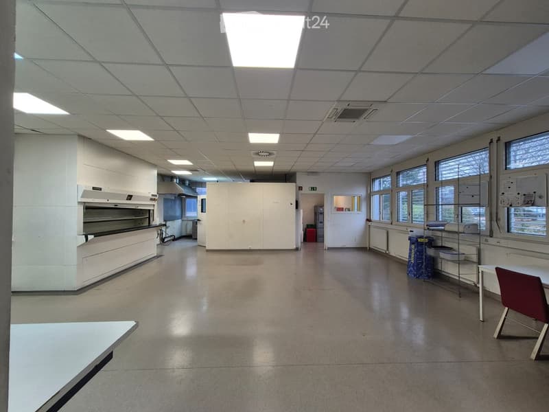 an empty room with tile flooring, large windows, industrial oven, a table, and a chair