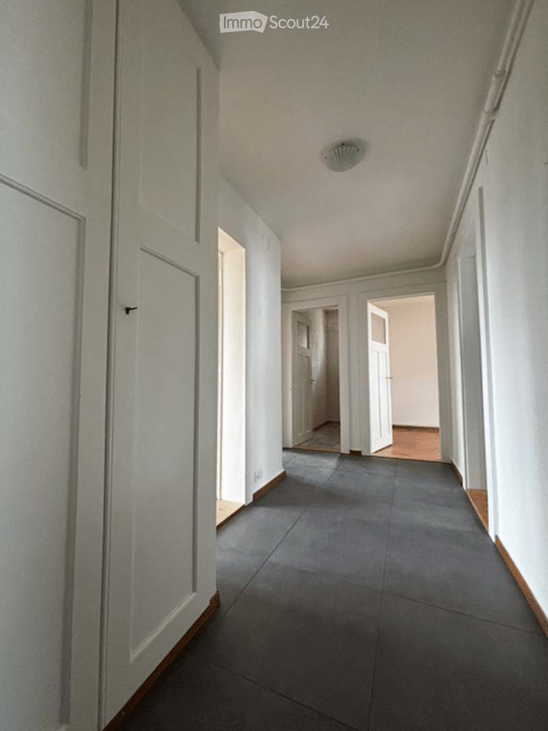 Empty hallway with white walls, dark grey tiled floor, and several white doors leading to other rooms.