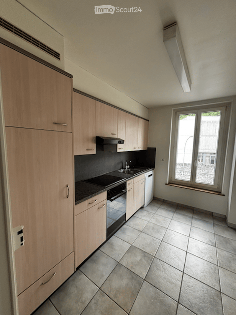 Modern kitchen with light wood cabinets, tiled floor, and built-in appliances including a sink, oven, and dishwasher.