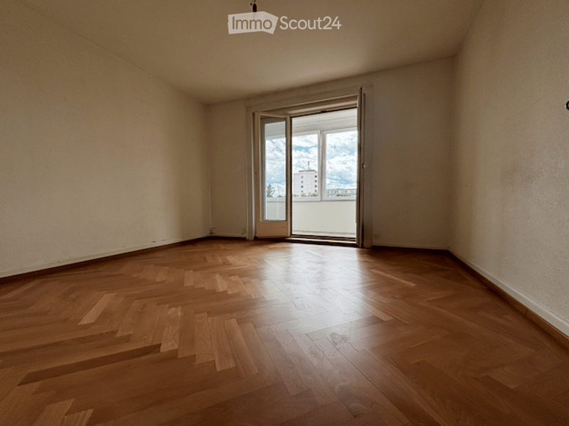 Empty room with wooden flooring and large sliding glass door leading to a balcony.