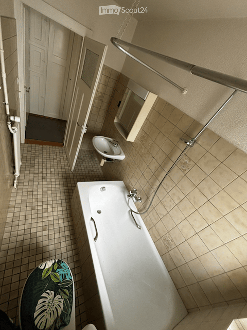 Bathroom with a white bathtub, a sink, a stool with a floral pattern, tiled walls and floor, and a mirror above the sink.