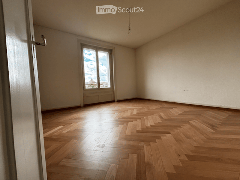 Empty room with wooden flooring and large window allowing natural light. No furniture or equipment present.