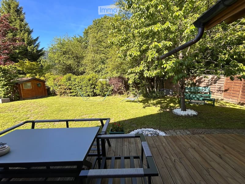 Well-maintained garden with a wooden deck, outdoor table and chairs, small shed, and a green bench in the background.
