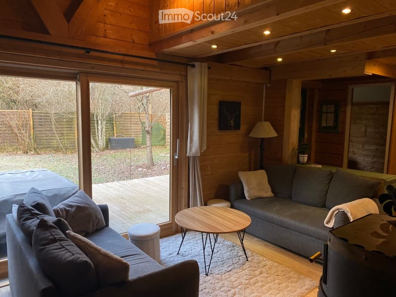 Cozy living room with wooden walls and ceiling, large window with view to the garden, two sofas, coffee table, floor lamp, and decorative items.