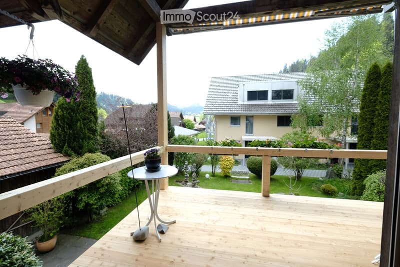 Balcony / Terrace. Wooden balcony with a small round table, potted plants, and a view of a well-maintained garden and neighboring houses.