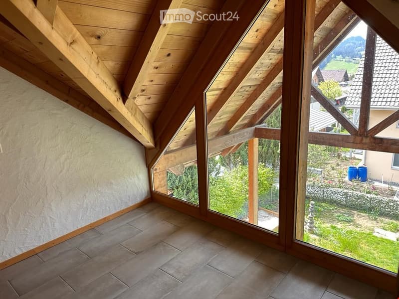 Unfurnished Room. Bright, unfurnished attic room with wooden beams, large windows offering a scenic view of the countryside, and tiled flooring.