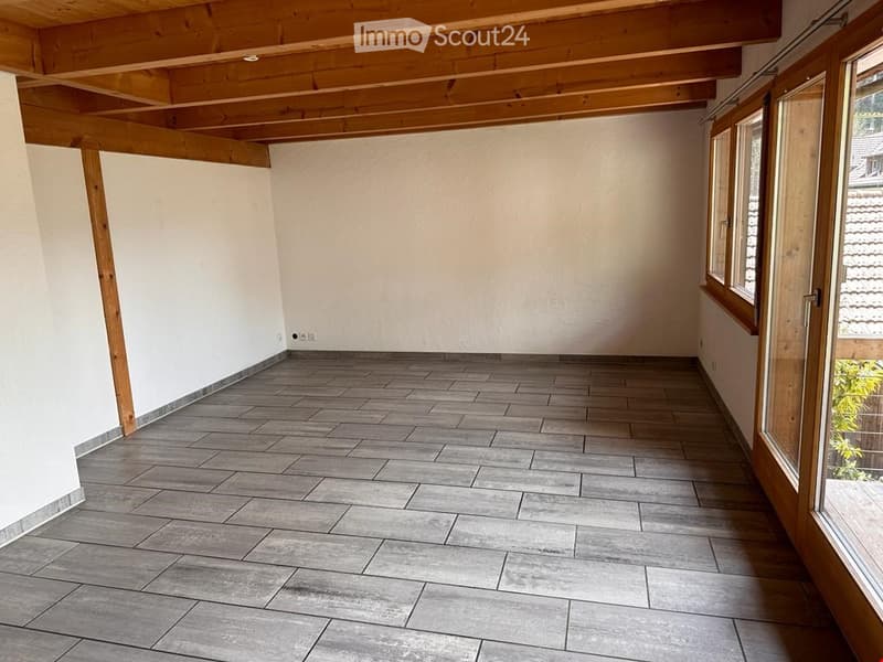 Unfurnished Room. Empty room with exposed wooden beams on the ceiling, grey tiled floor, and large windows with wooden frames.