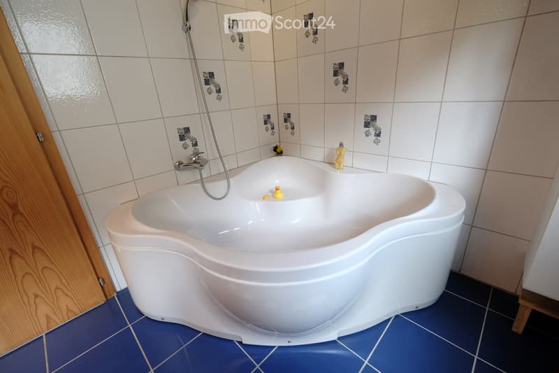Bathroom. Modern bathroom with a large, corner bathtub, tiled walls, and blue tiled floor. The bathtub features a modern faucet and showerhead, with two small toys inside.