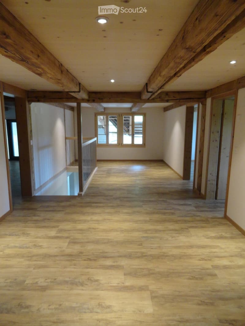 Corridor / Hallway. Empty hallway with wooden flooring, exposed wooden beams, and a staircase leading to another level.