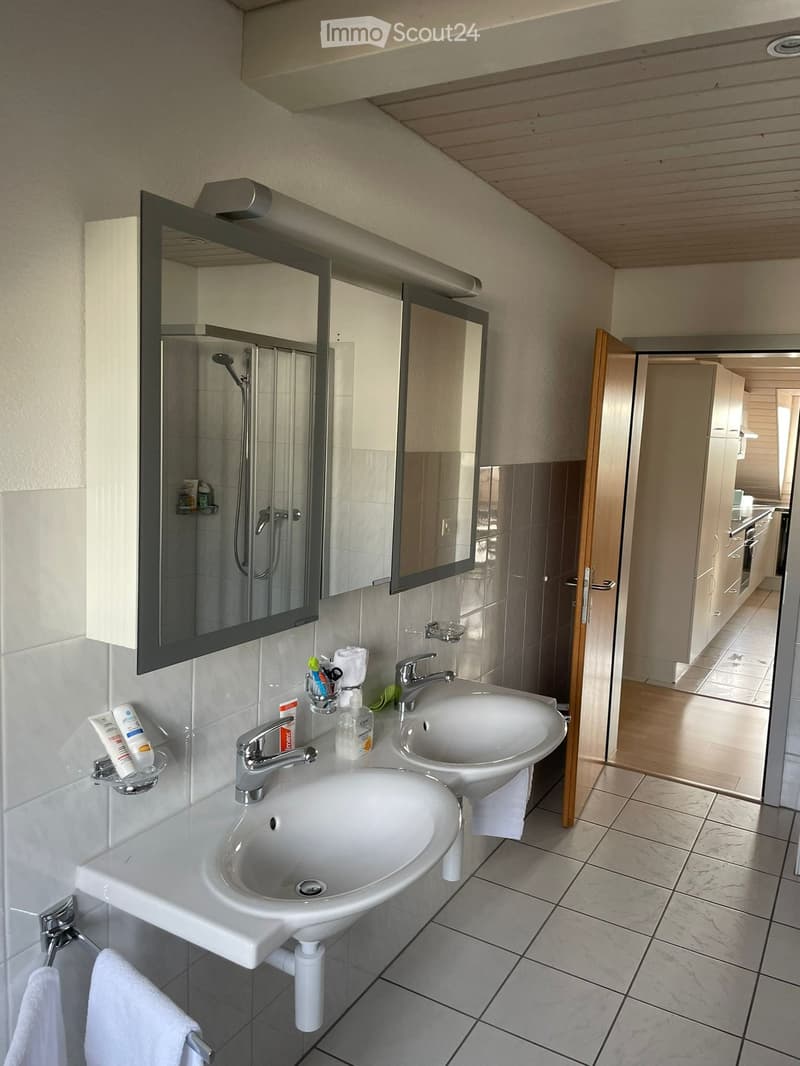 white tiled walls, modern double sink, faucets, mirrors with a shower enclosure, a towel rack, open door