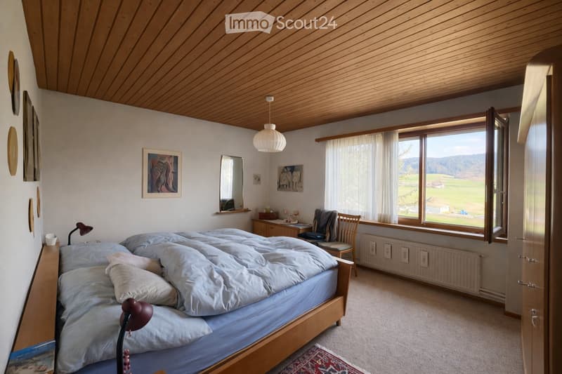 Cozy bedroom with a large bed, wooden furniture, large windows with a scenic view, and artwork on the walls.