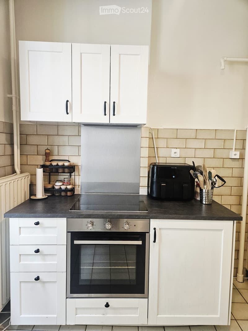 Modern kitchen with white cabinets, black countertop, stainless steel oven, induction stove, and various appliances and utensils.