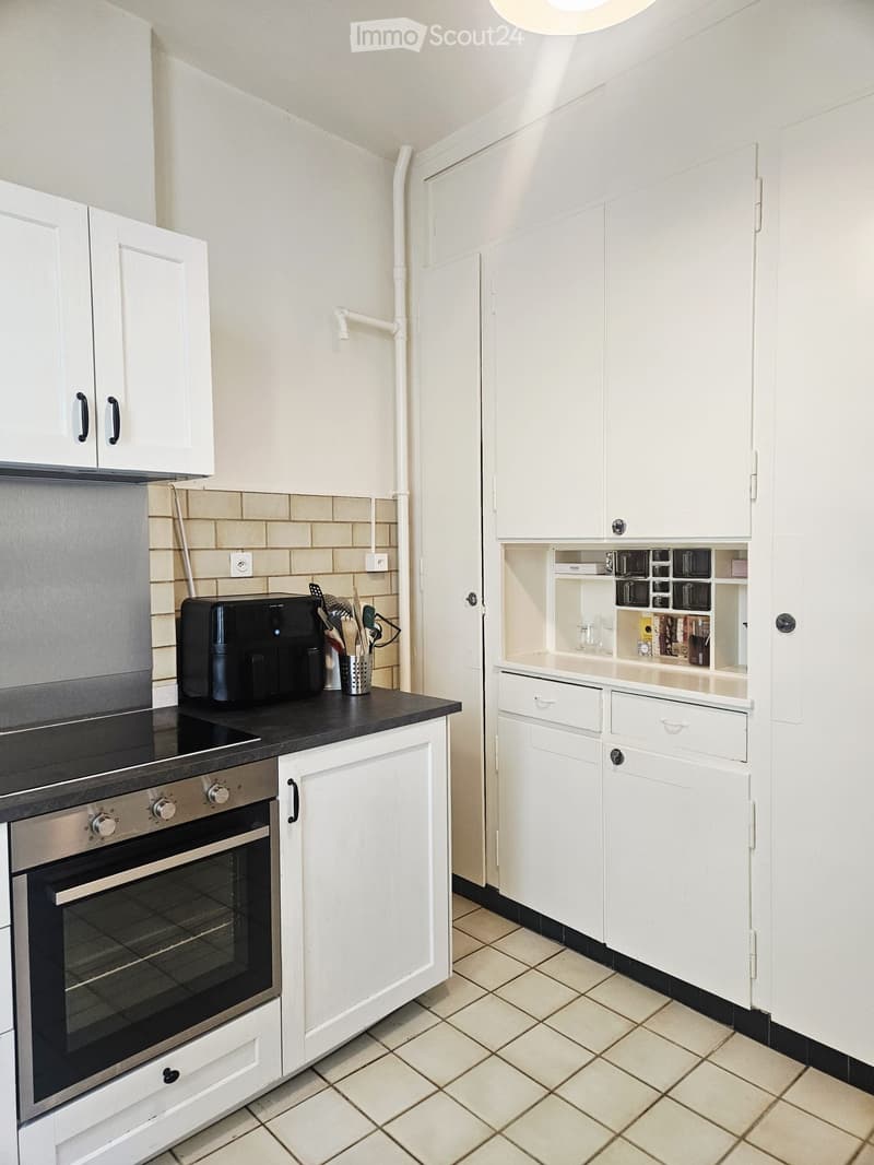 Modern kitchen with white cabinets, stainless steel oven, coffee maker, and tiled floor.