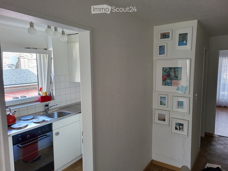 Modern kitchen with white cabinets, stainless steel sink, red teapot, and framed pictures on the wall.