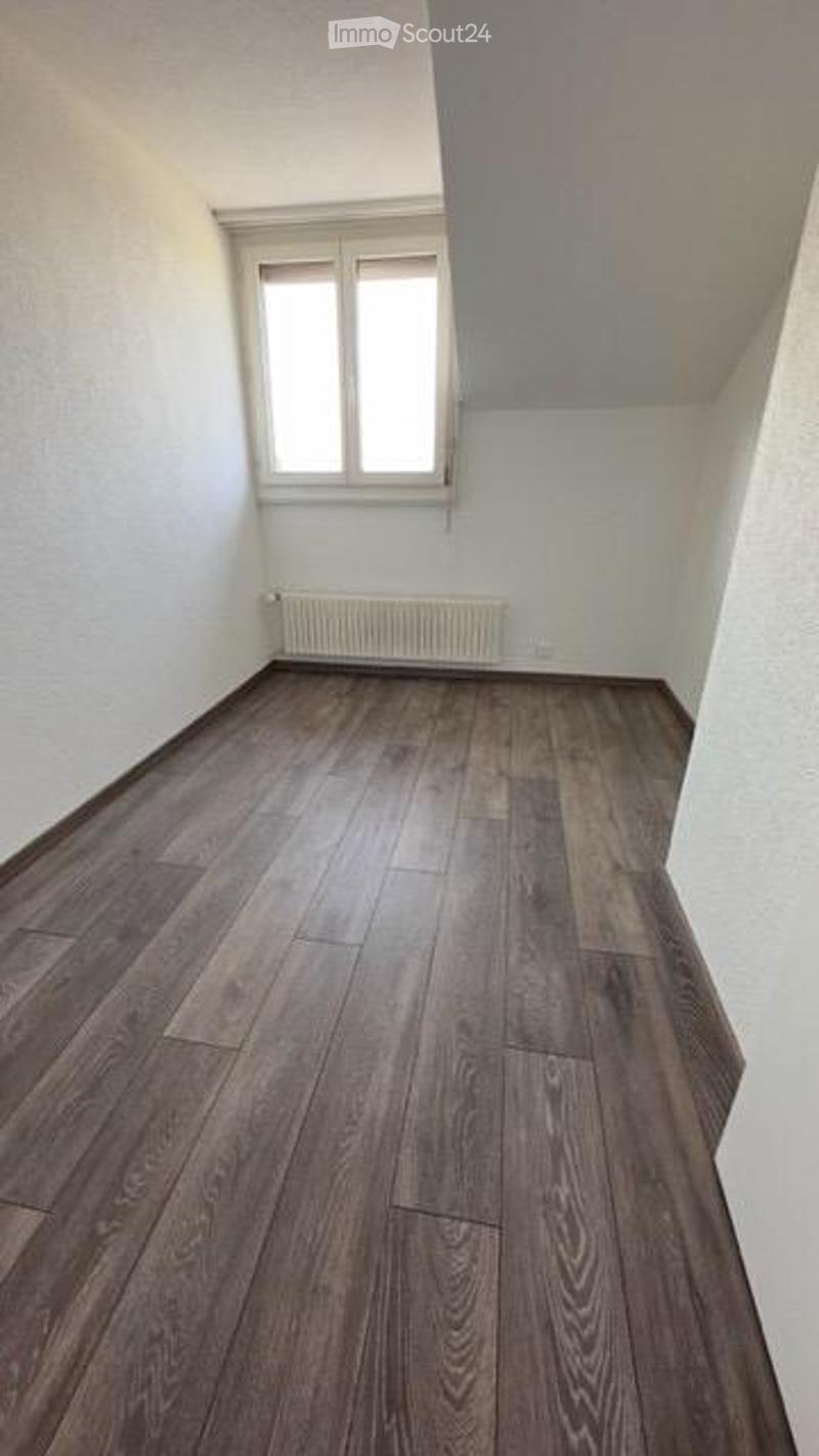 Empty room with wooden flooring, white walls, and a single window with white frame. Radiator visible below the window.