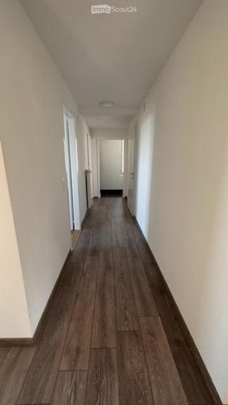 Empty hallway with wooden flooring, white walls, and a closed door at the end.