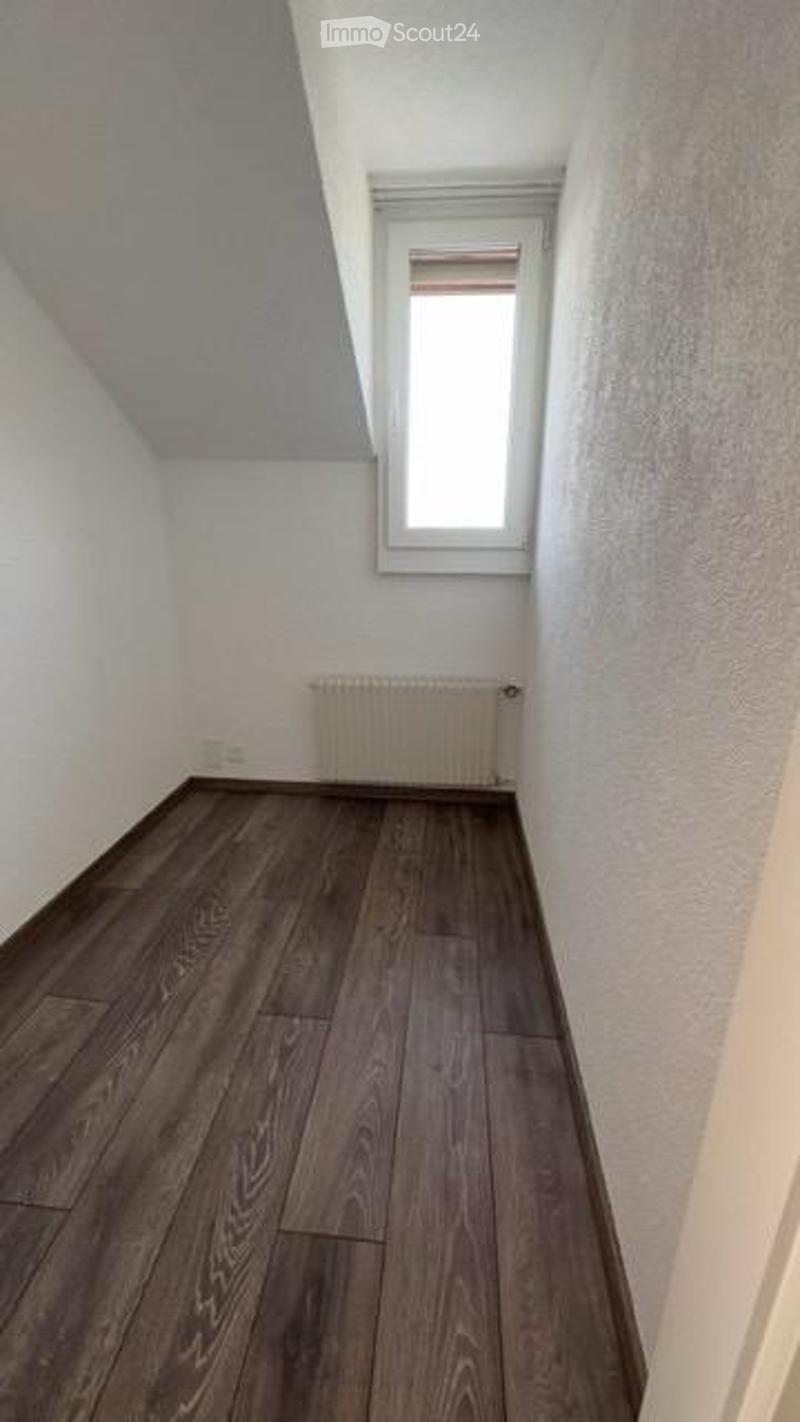 Completely empty room with wooden flooring, white walls, and a single window with blinds. A radiator is visible below the window.