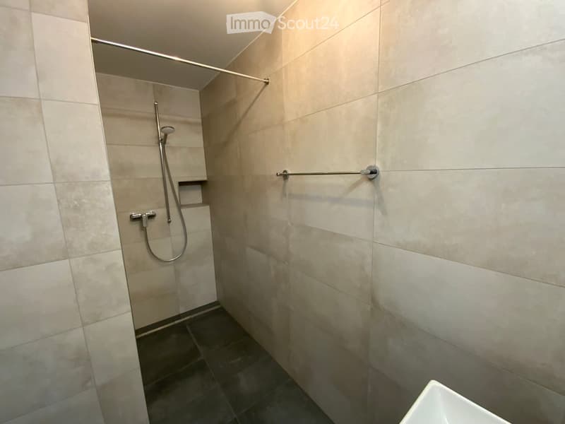 Modern shower area with beige tiles, a handheld showerhead, and a towel rack.