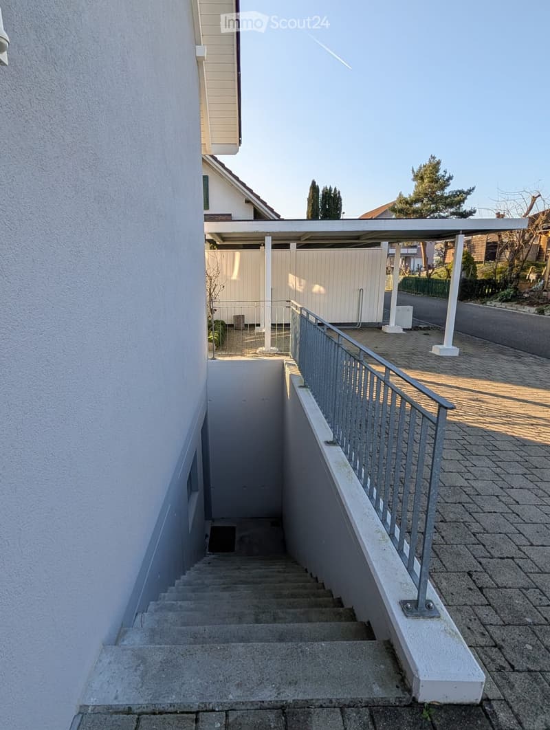 Concrete stairs leading to the ground floor entrance, metal railing, white wall