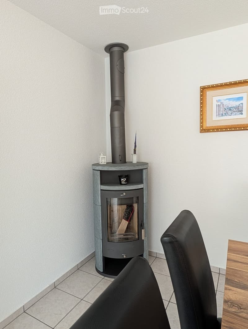 A cozy corner with a fireplace, white wall, wooden chair, small table, picture frame, and decorative objects.