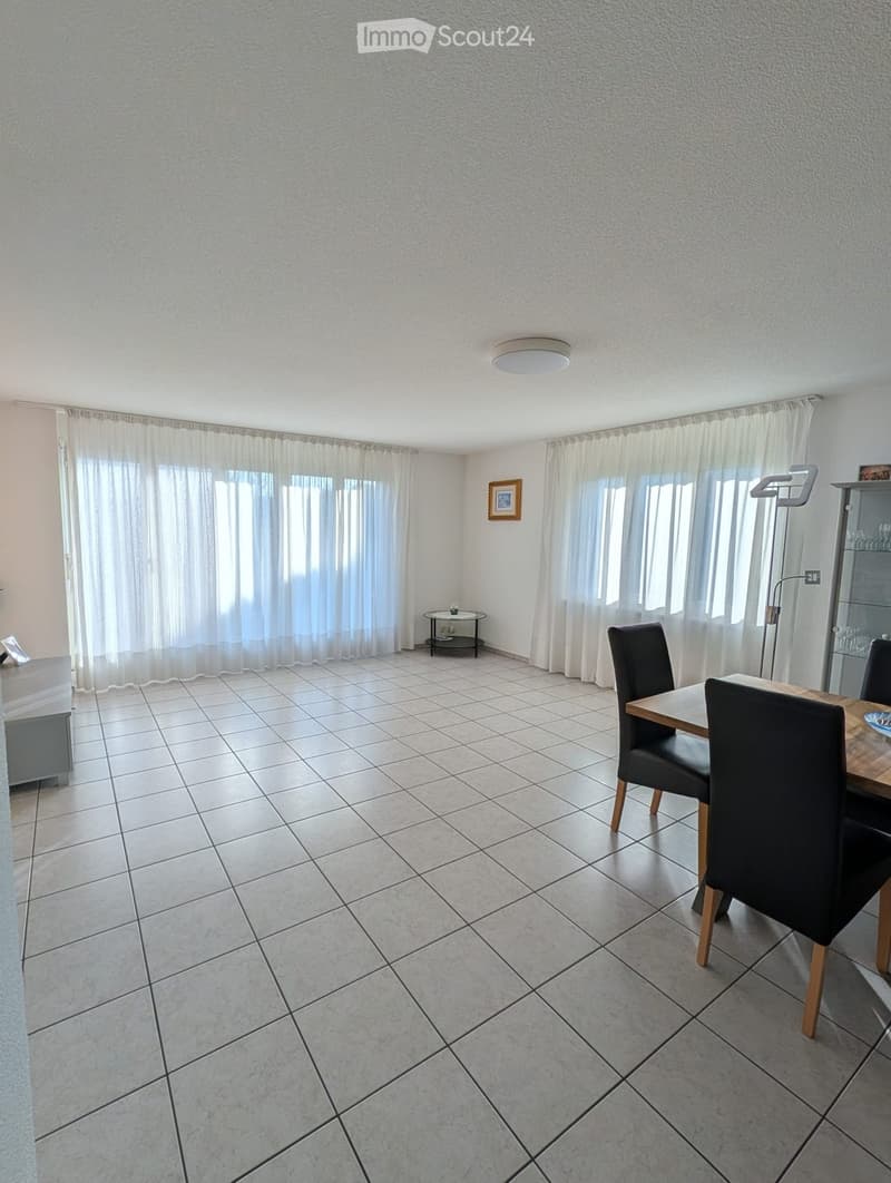 Empty room with white tiles, dining table with 4 chairs, wall mounted frame, windows with white curtains