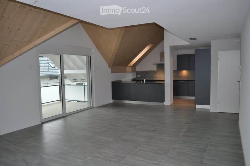 Modern, open-plan living and kitchen area with dark grey tiles, sleek kitchen cabinets, and a sliding glass door leading to a balcony.