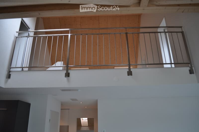 Modern interior view of a spacious hallway with a wooden ceiling and a metal railing leading to an upper level. The walls are painted white, and the floor appears to be light-colored wood or laminate.