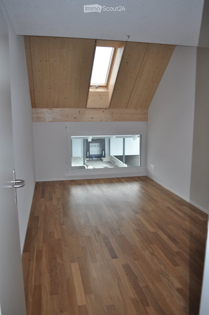 Empty room with wooden flooring, white walls, and a skylight window at the top. A mirror on the wall reflects part of another room.
