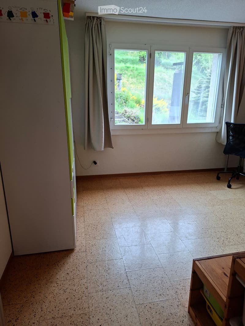 Empty room with tiled floor, large windows with curtains, and a small wooden shelf in the corner.