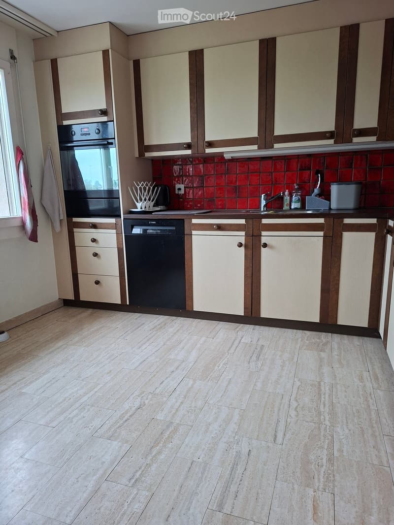 Modern kitchen with light-colored cabinets, a red-tiled backsplash, and a marble-effect tiled floor. Features an oven, dishwasher, sink, and various small appliances.