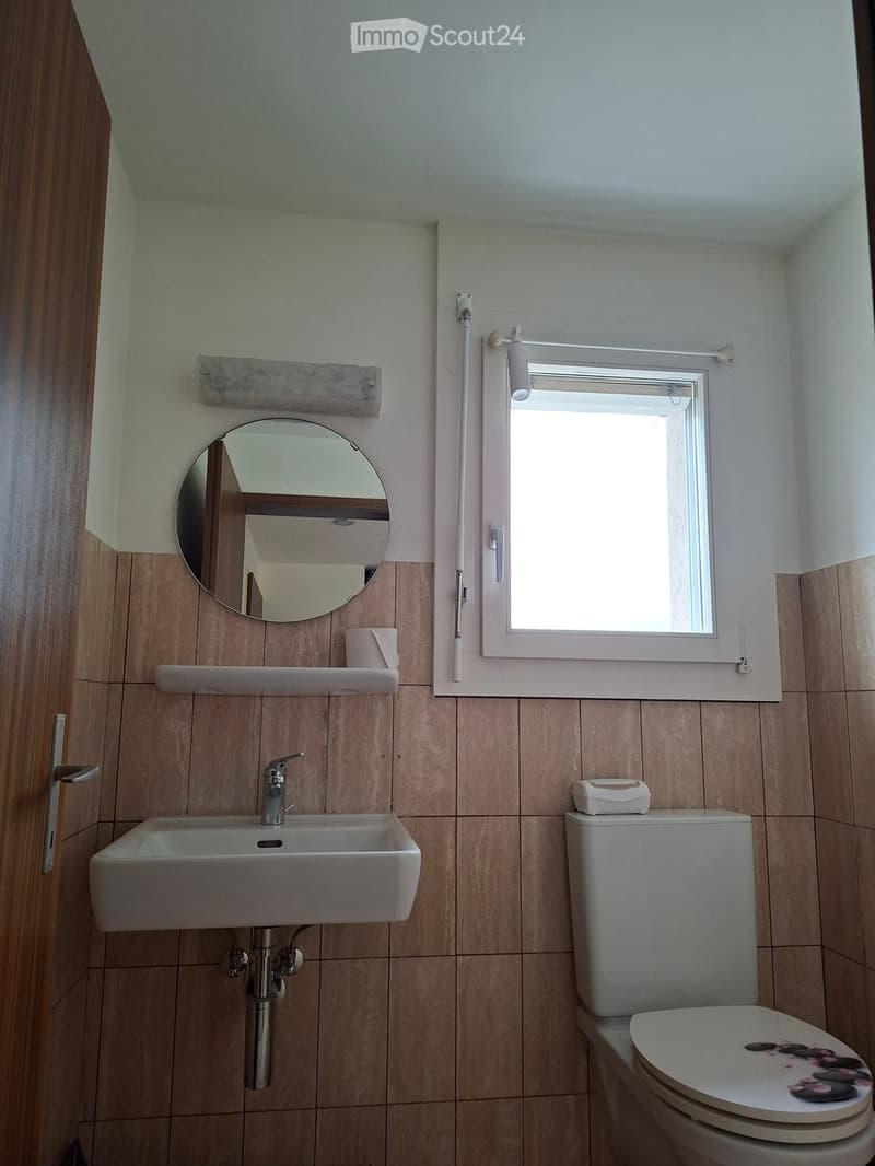 Bathroom with a white sink, chrome faucet, toilet with a floral cover, round mirror, and a window with blinds.