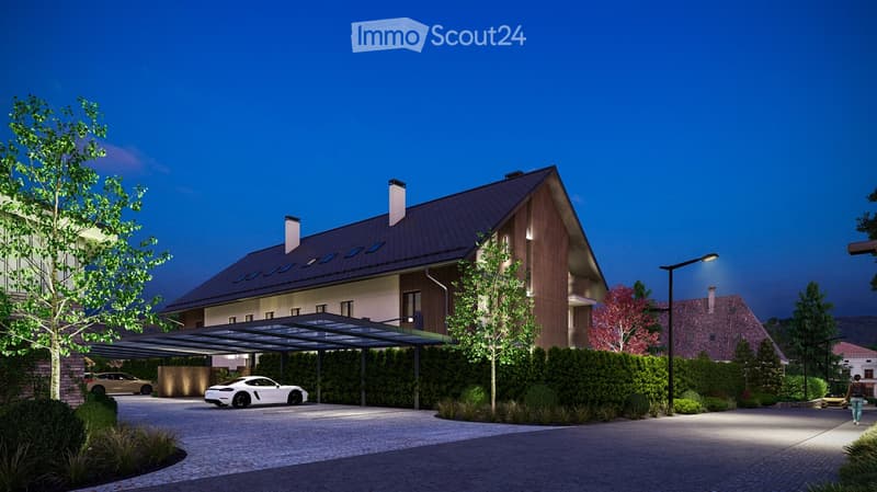 Modern two-story house with a sloped roof, wooden facade, and covered driveway. Features include a garage, landscaped garden, and parked cars.
