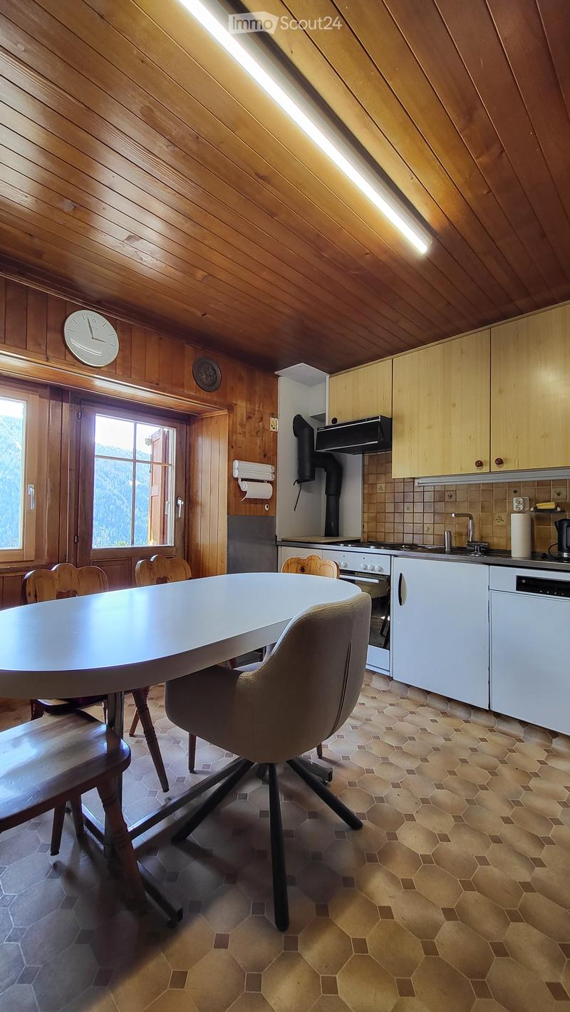 Bright kitchen with wooden walls and ceiling, featuring a round dining table with chairs, modern appliances including a refrigerator, oven, and sink, and ample natural light from a large window.